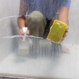 A picture of someone cleaning limescale off a shower screen due to hard water