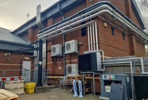 A picture of the outside of a sports centre with air source heat pumps and other appliances on the wall